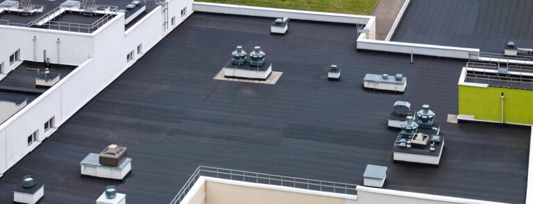 Draufsicht auf dunkles Flachdach mit Klimaanlagen und Hydroisolationsmembranen, moderne Wohngegend für Mehrfamilienhäuser.